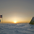 南極日出(2008)說明翻譯自NASA地球觀測網站說明文字.冰凍的景象中,一面邊緣破損的美國國旗飄揚在標示南極點的指標上.