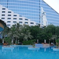 位於波斯灣畔的Jumeirah Beach Hotel，泳池畔綠樹搖曳，玻璃牆上映著帆船飯店Burj Al Arab的倩影