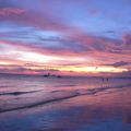 落日餘暉在雲端落腳，亮著緋紅、藍紫的光芒，映著海水，和弧形的海灣鉤勒出絕美的線條、光影與色彩。